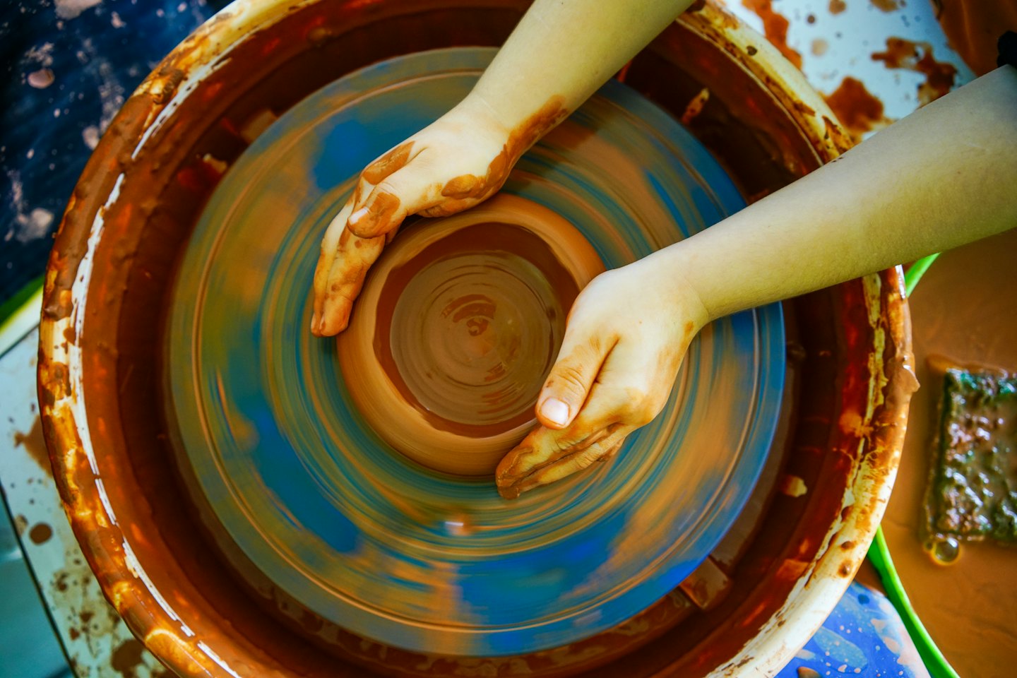 Hands shaping wet clay on a spinning pottery wheel.