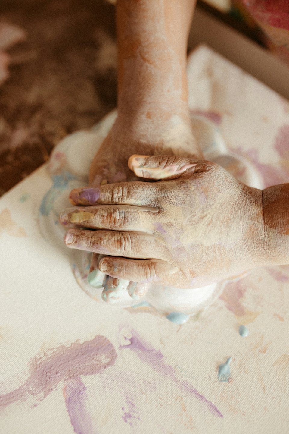 Hands smudged with pastel paints pressing into soft material.