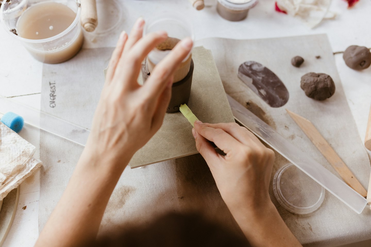 Hands shaping clay on a canvas mat with pottery tools.