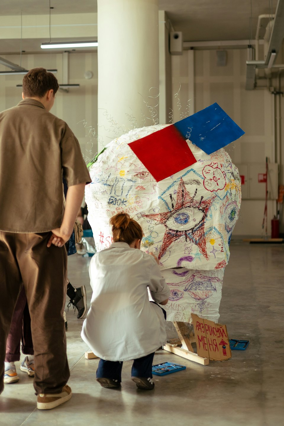 Two people collaborate on a large artistic sculpture in a studio.